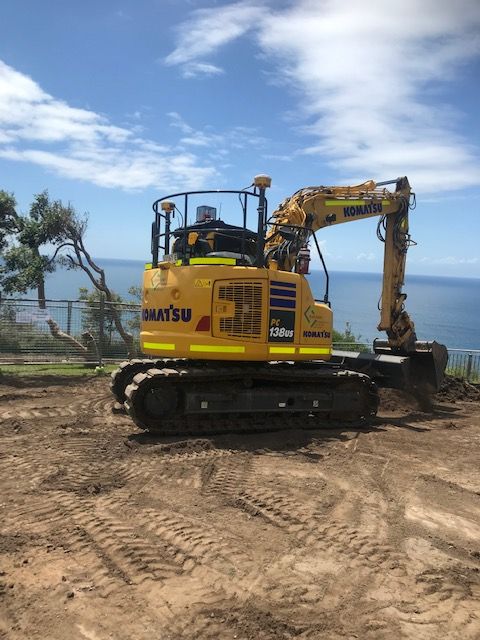 A yellow excavator is parked in a dirt field near the ocean. — Adam Lowe Earthmoving Pty Ltd in Somersby, NSW