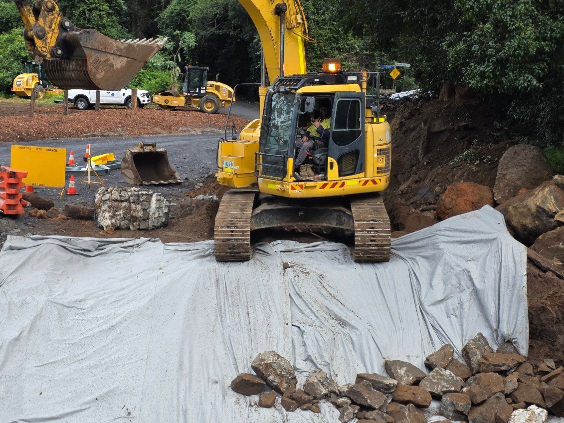 A yellow excavator is moving rocks on a construction site — Adam Lowe Earthmoving Pty Ltd in Somersby, NSW