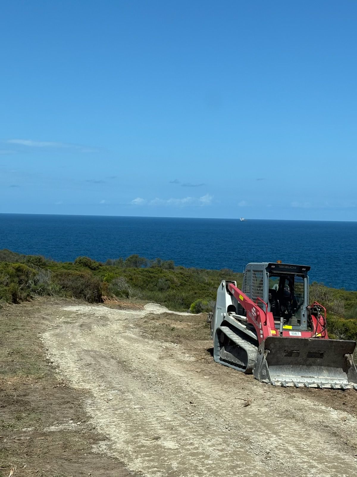 A bulldozer is parked on a dirt road next to the ocean. — Adam Lowe Earthmoving Pty Ltd in Somersby, NSW