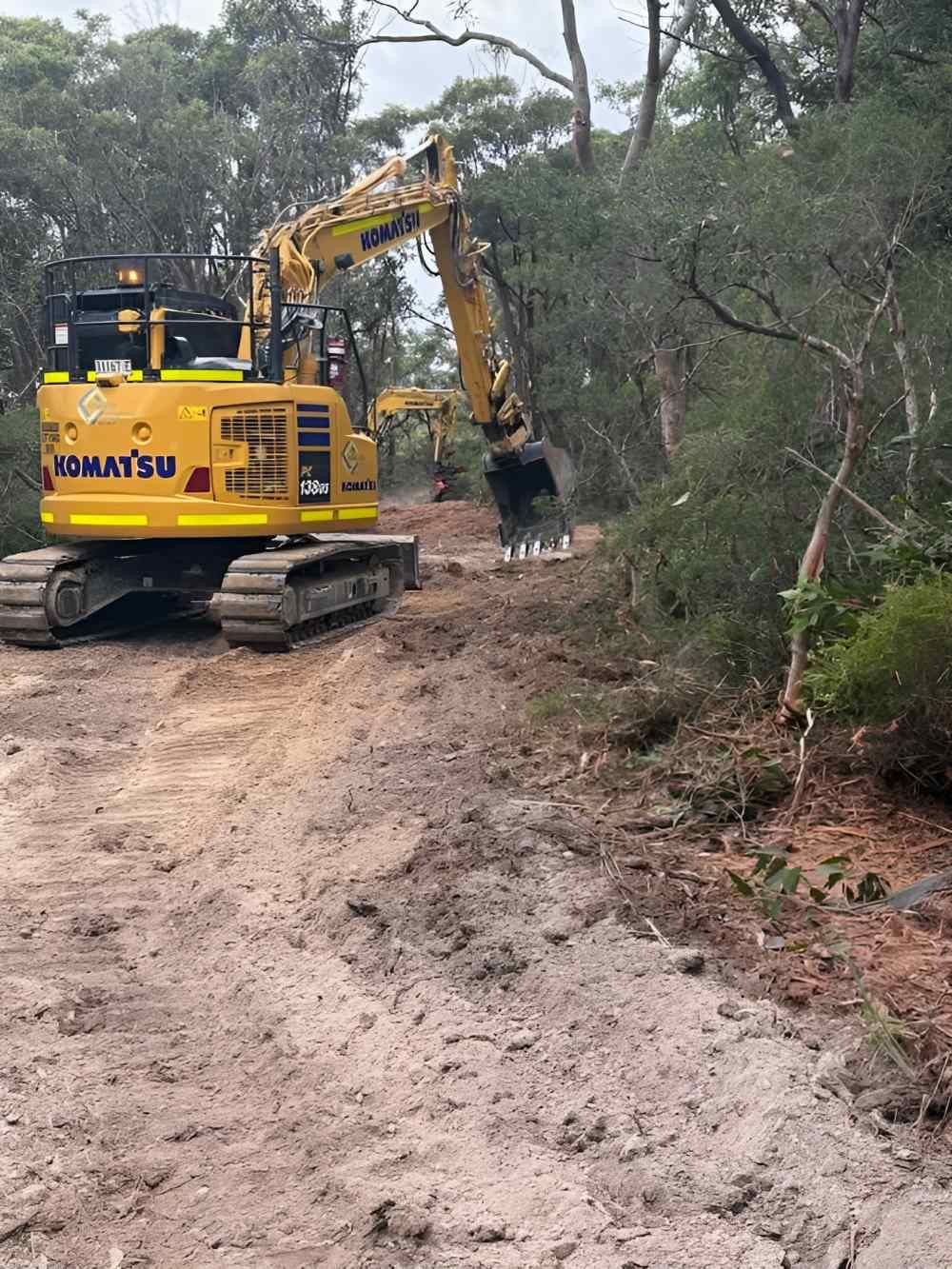 A Yellow Excavator Is Driving Down a Dirt Road — Adam Lowe Earthmoving Pty Ltd in Somersby, NSW