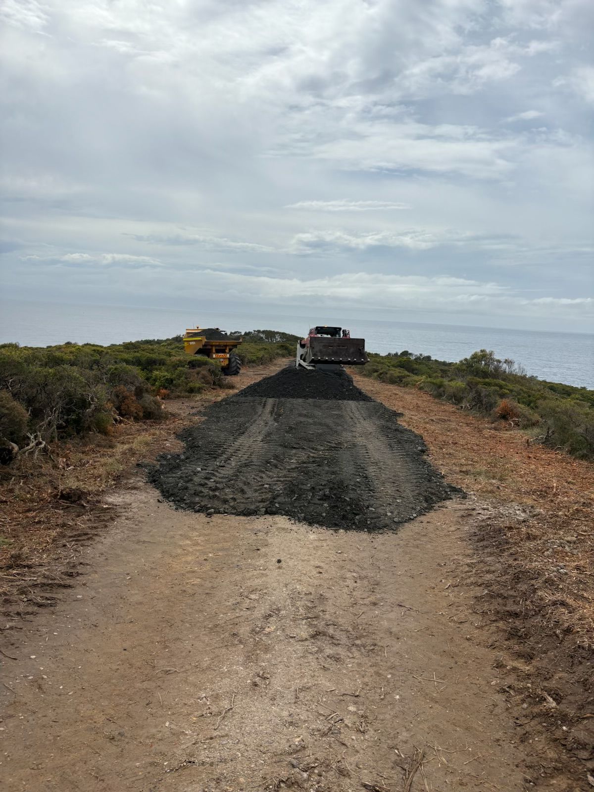 A truck is driving down a dirt road next to the ocean. — Adam Lowe Earthmoving Pty Ltd in Somersby, NSW