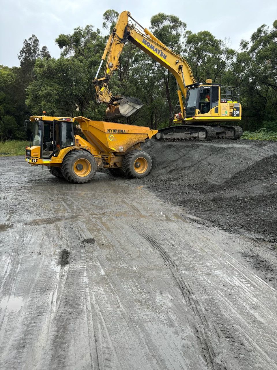 A yellow excavator is loading a dump truck with dirt. — Adam Lowe Earthmoving Pty Ltd in Somersby, NSW