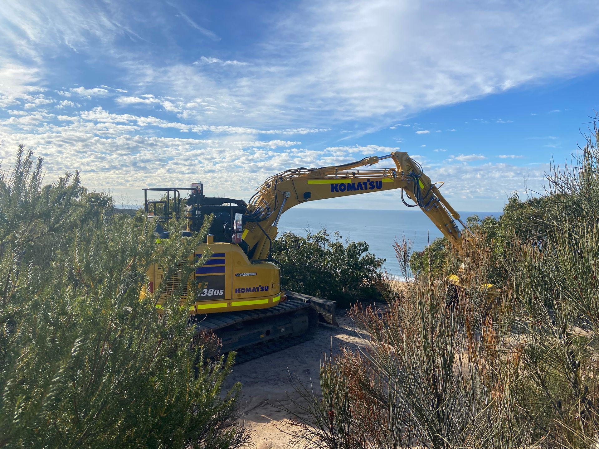 A yellow excavator is sitting on top of a hill next to a body of water. — Adam Lowe Earthmoving Pty Ltd in Somersby, NSW