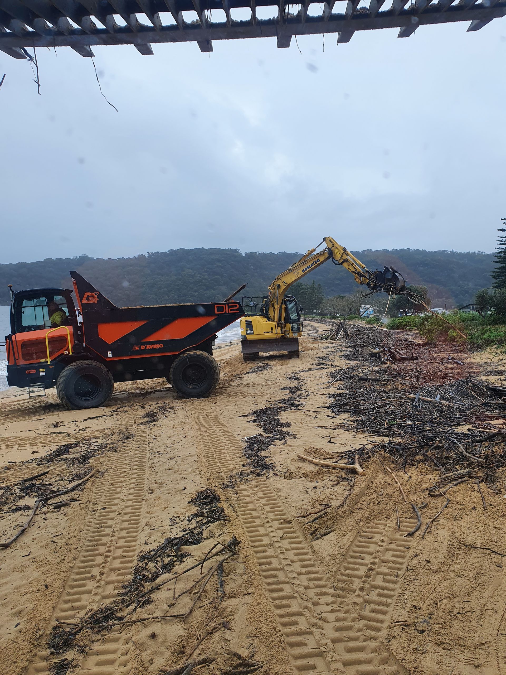 A dump truck is driving down a dirt road next to a yellow excavator. — Adam Lowe Earthmoving Pty Ltd in Somersby, NSW
