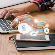 Persona escribiendo en una computadora portátil, con íconos de seguridad digital superpuestos en un teléfono inteligente y una computadora portátil.