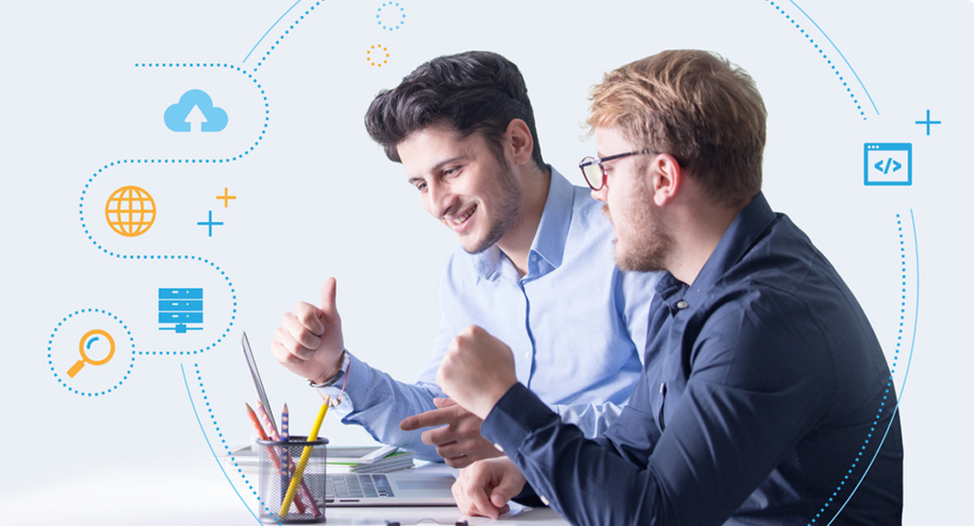 Dos hombres sonriendo, colaborando en un escritorio, rodeados de íconos tecnológicos, fondo claro.