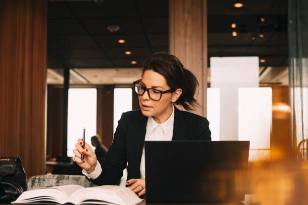 A woman is sitting at a desk with a laptop and a book.