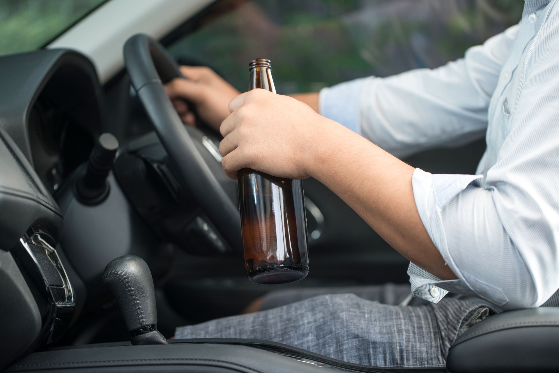 A man is holding a bottle of beer while driving a car.