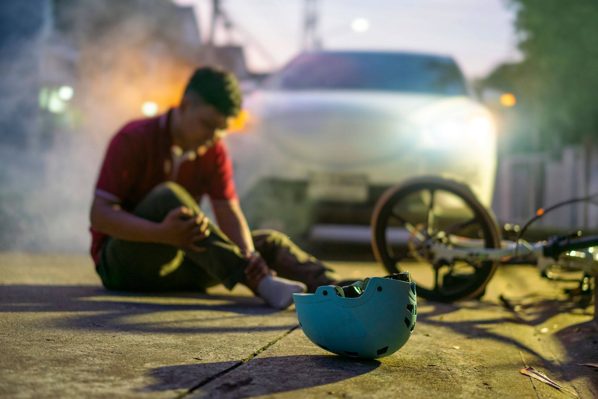 A man is sitting on the ground next to a bicycle and a car.