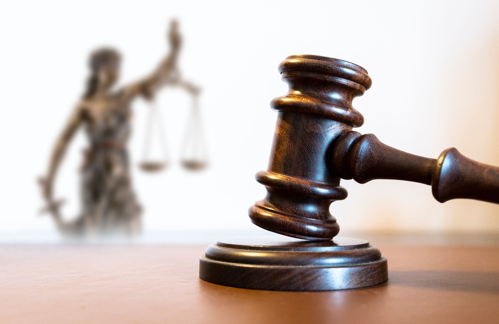 A wooden judge's gavel is on a table with a statue of justice in the background.