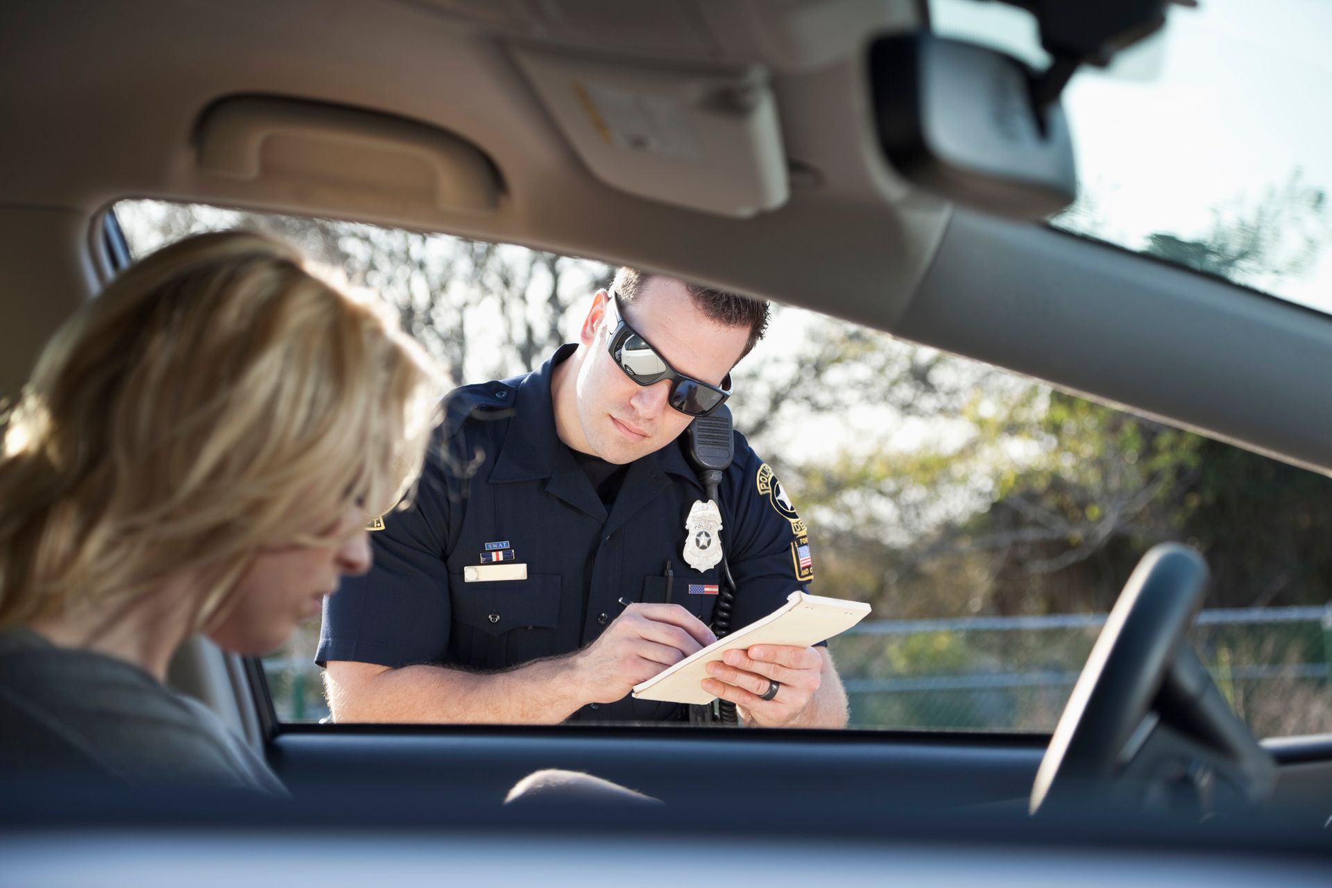 A police officer is writing a ticket to a woman in a car.