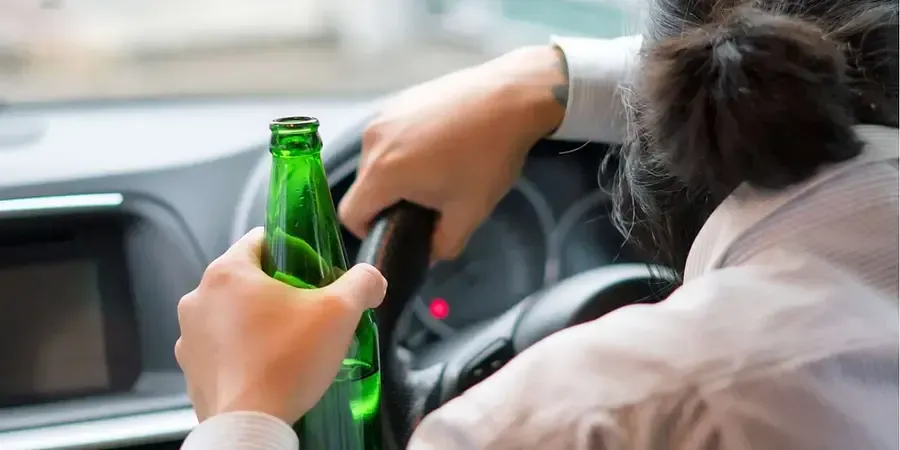 A woman is holding a bottle of beer while driving a car.