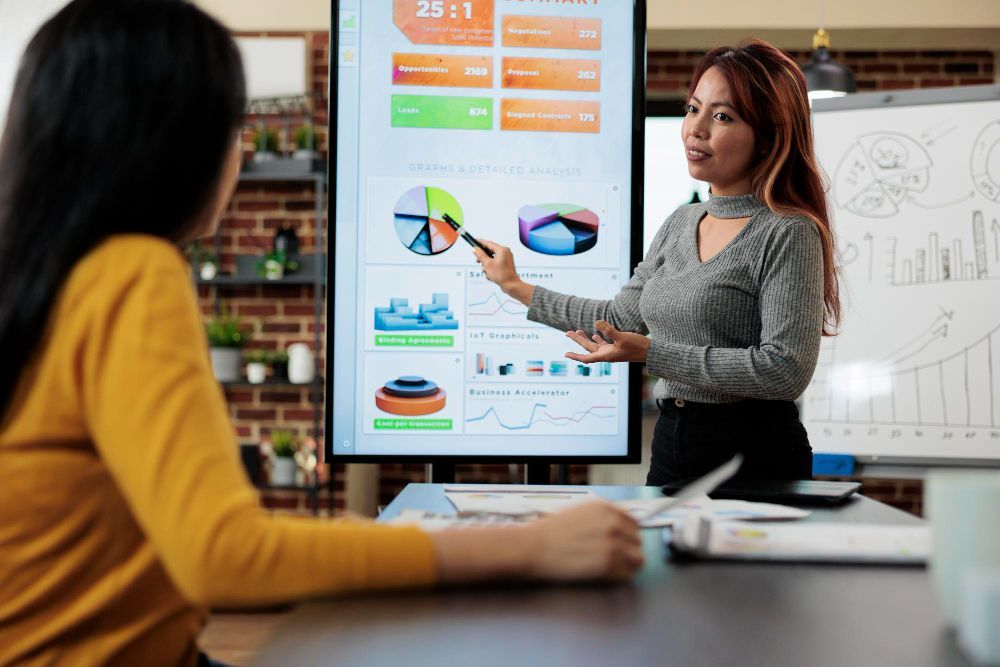 A woman is giving a presentation to another woman in front of a large screen.