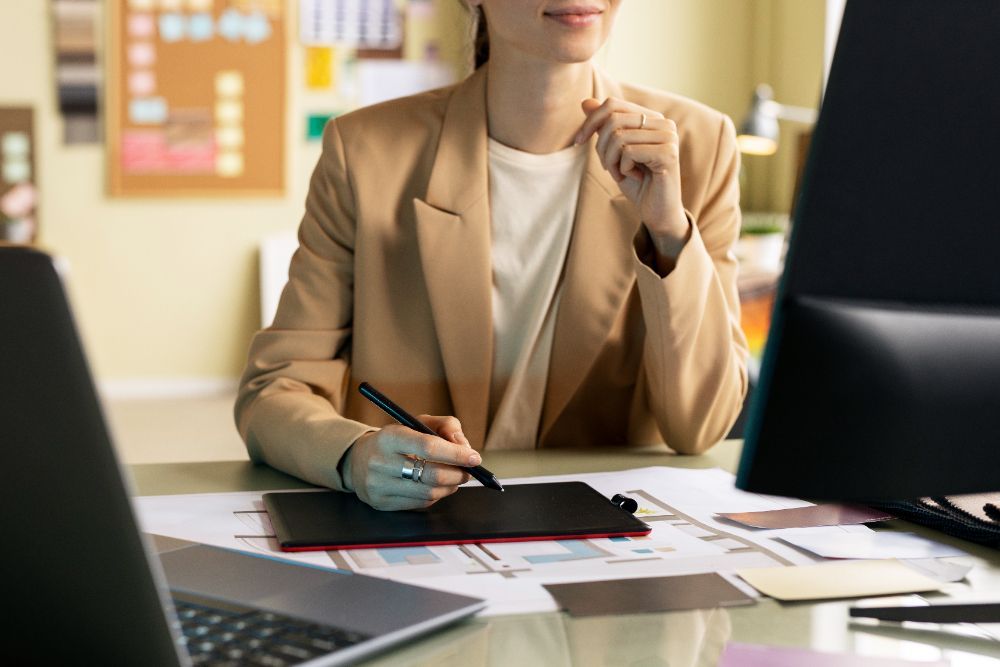 A woman is sitting at a desk using a graphic tablet.