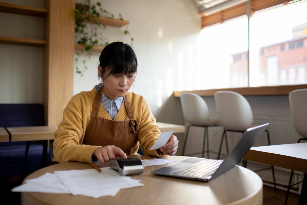 A woman is sitting at a table with a laptop and a calculator.