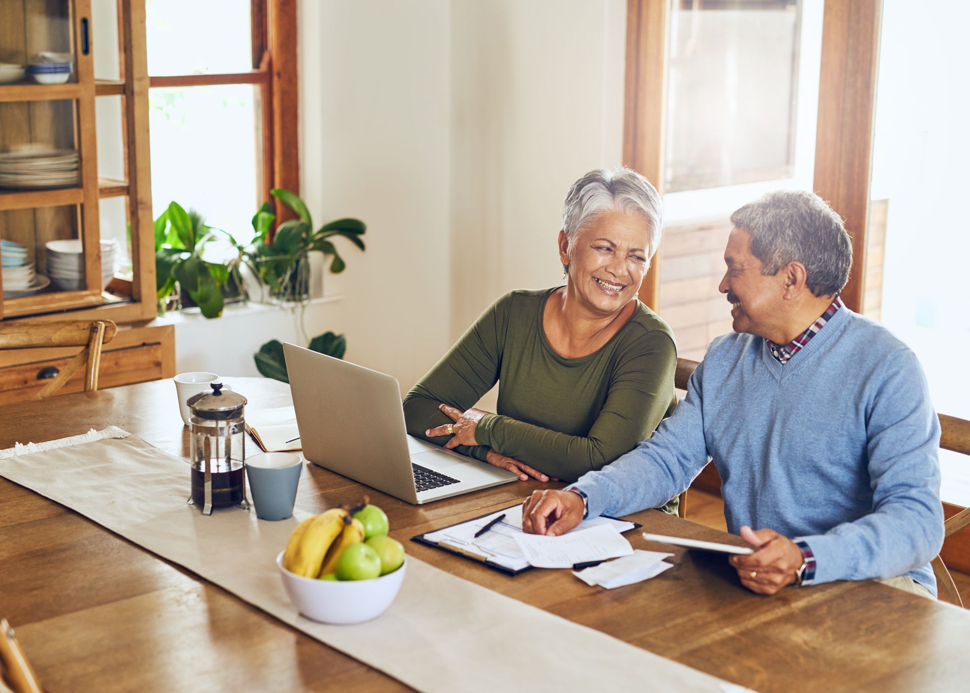 An elderly couple is sitting at a table using a laptop computer.