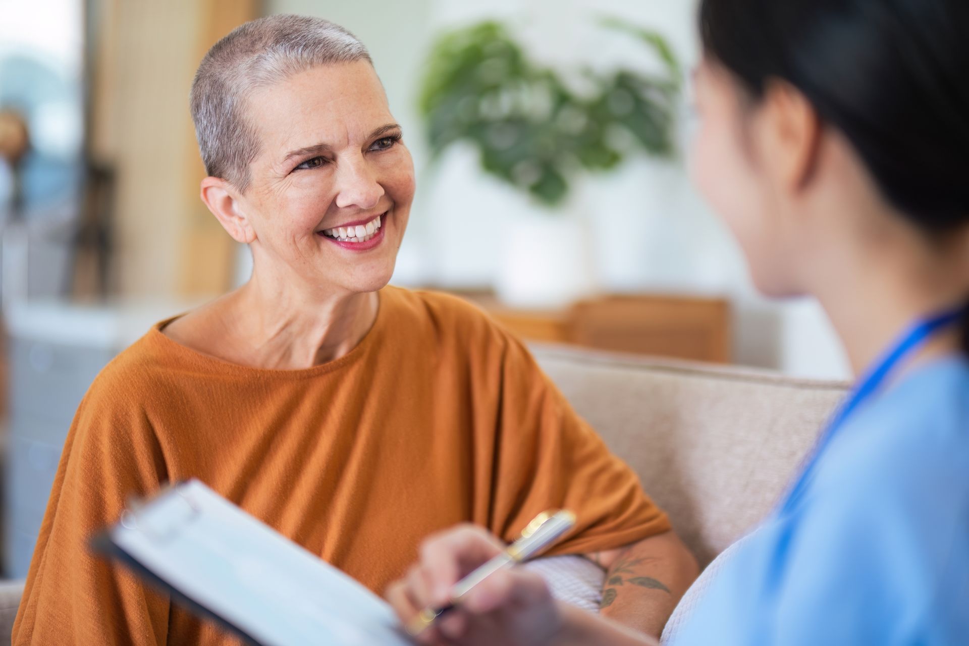 A woman with cancer is sitting on a couch talking to a nurse.