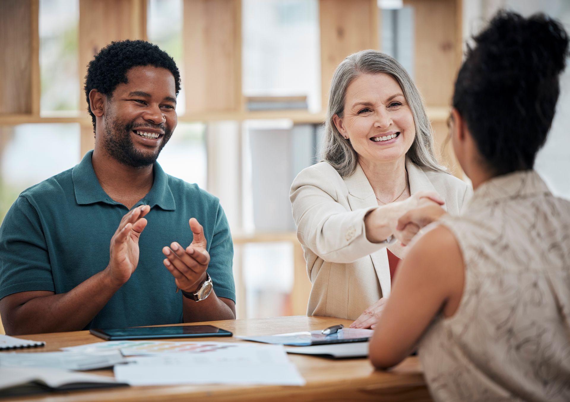 A man and a woman are shaking hands while sitting at a table.