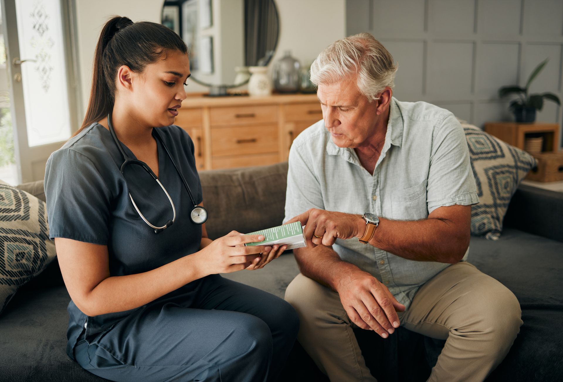 A nurse is talking to an elderly man on a couch.