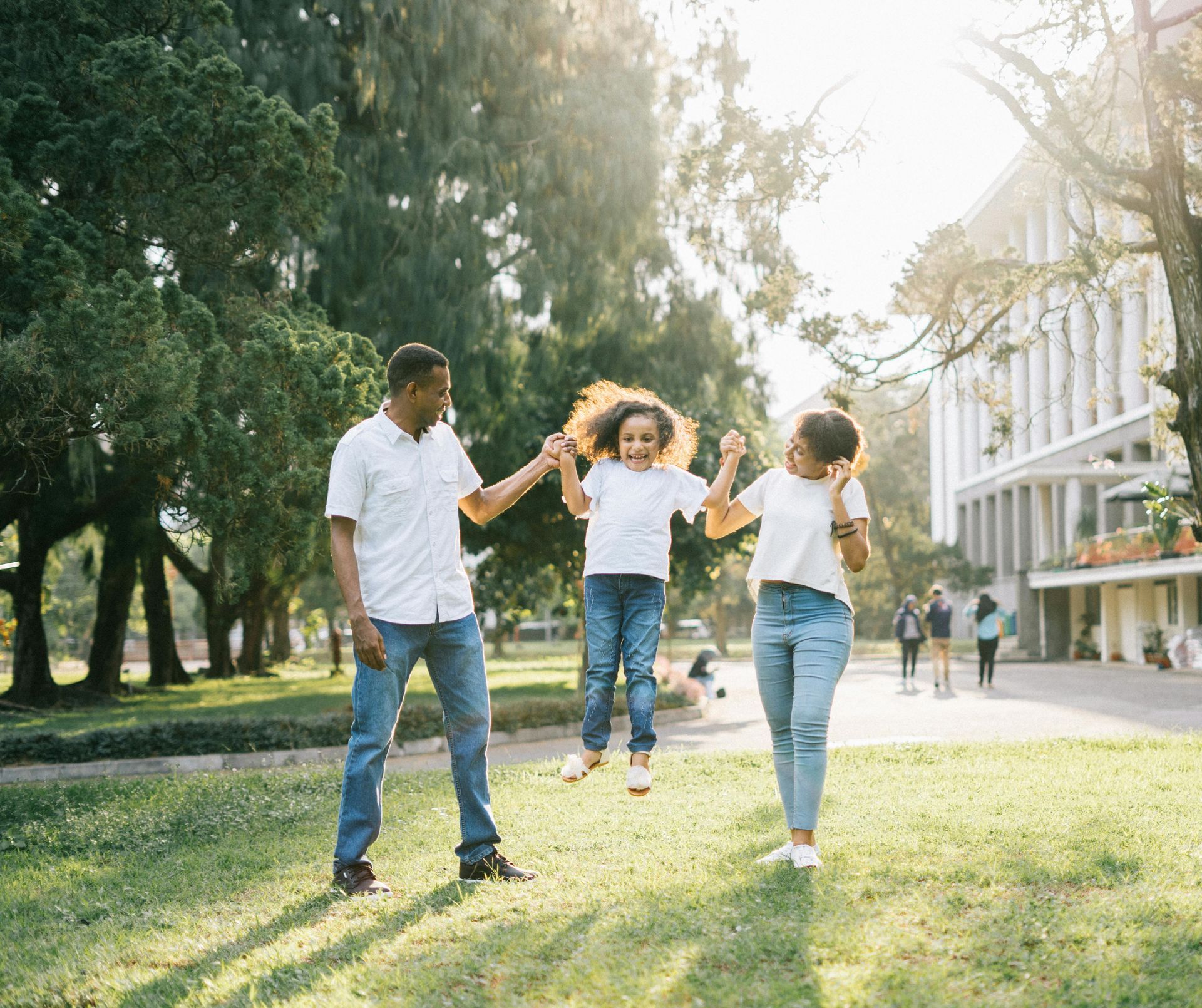 A family is holding hands and jumping in the air in a park.