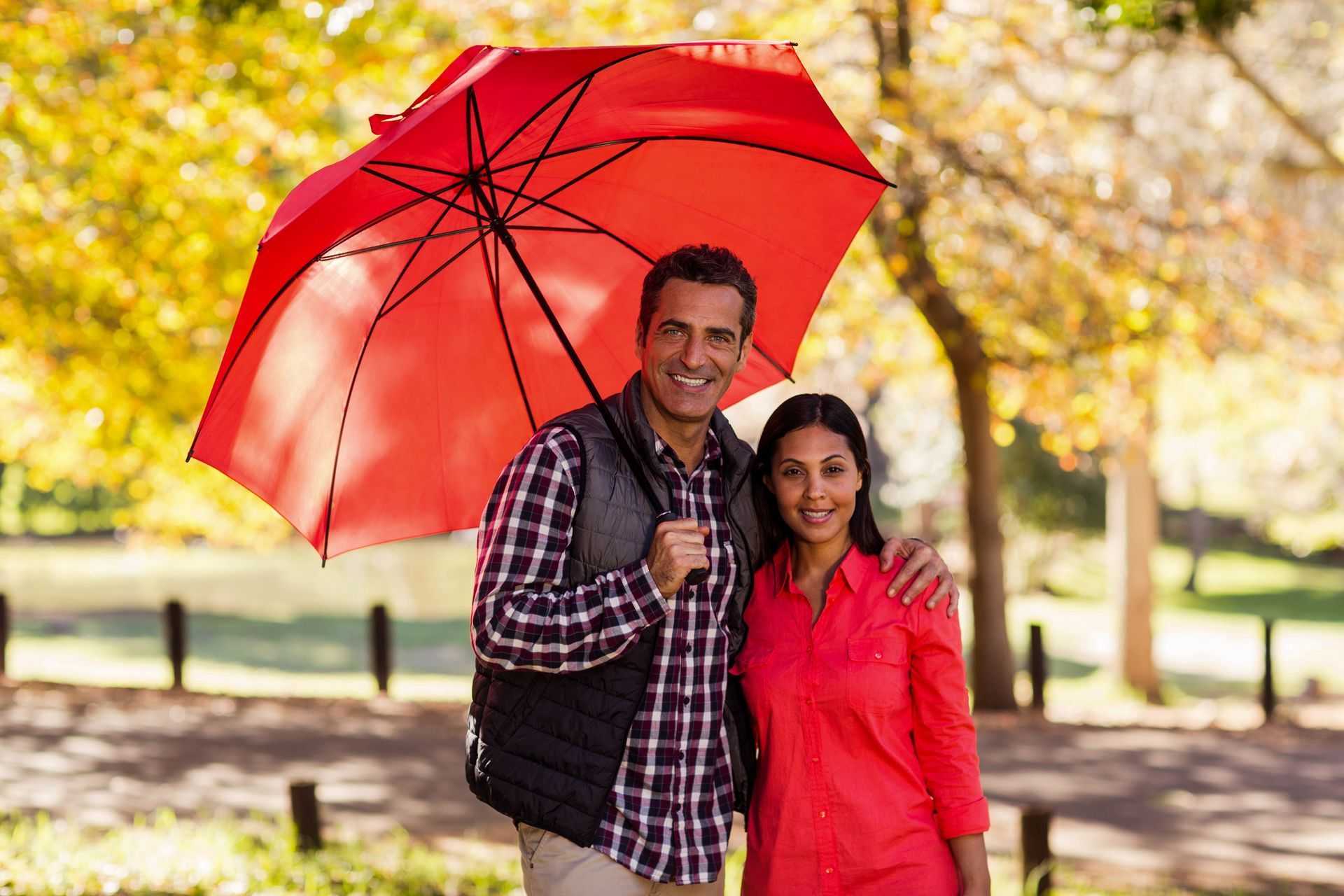 A man is holding a red umbrella over a woman in a park.