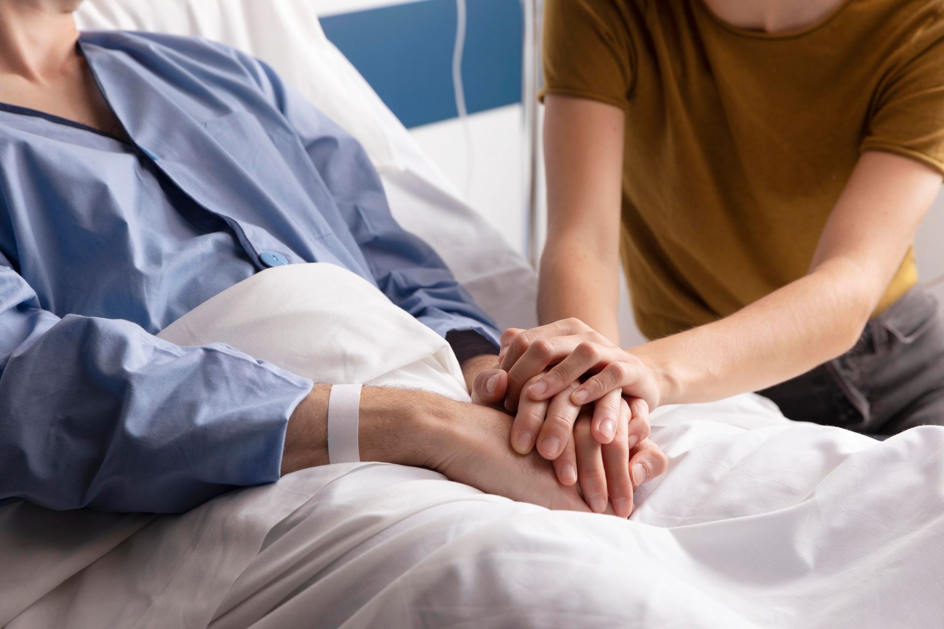 A woman is holding the hand of a patient in a hospital bed.