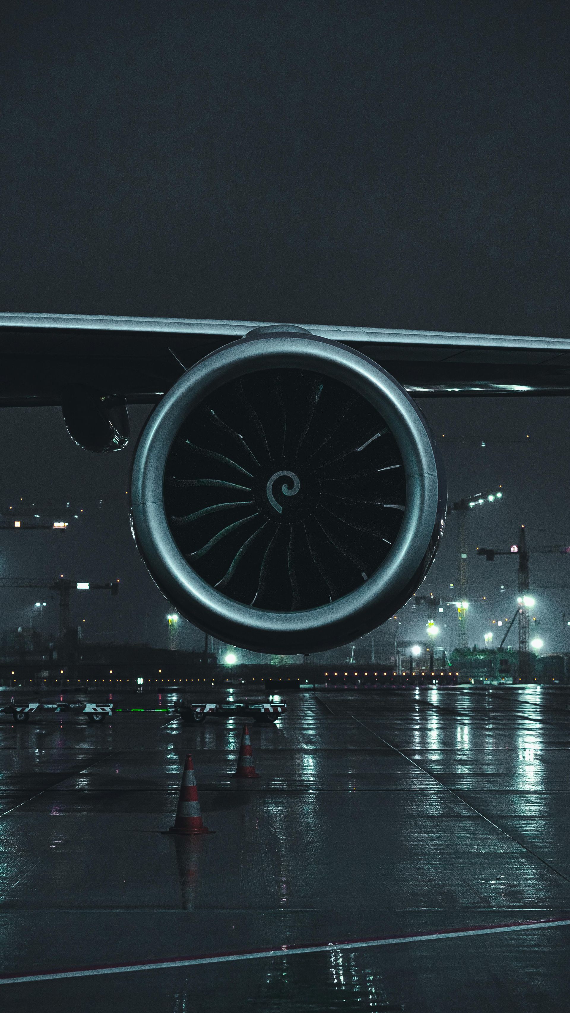 Airplane engine on wet tarmac at night; city lights in the distance.