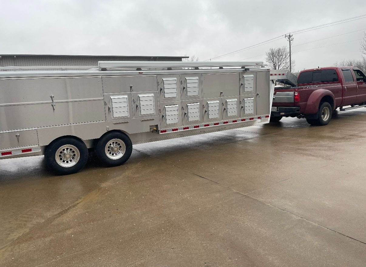 Red truck towing a long silver trailer with several white compartments on a wet, concrete surface.