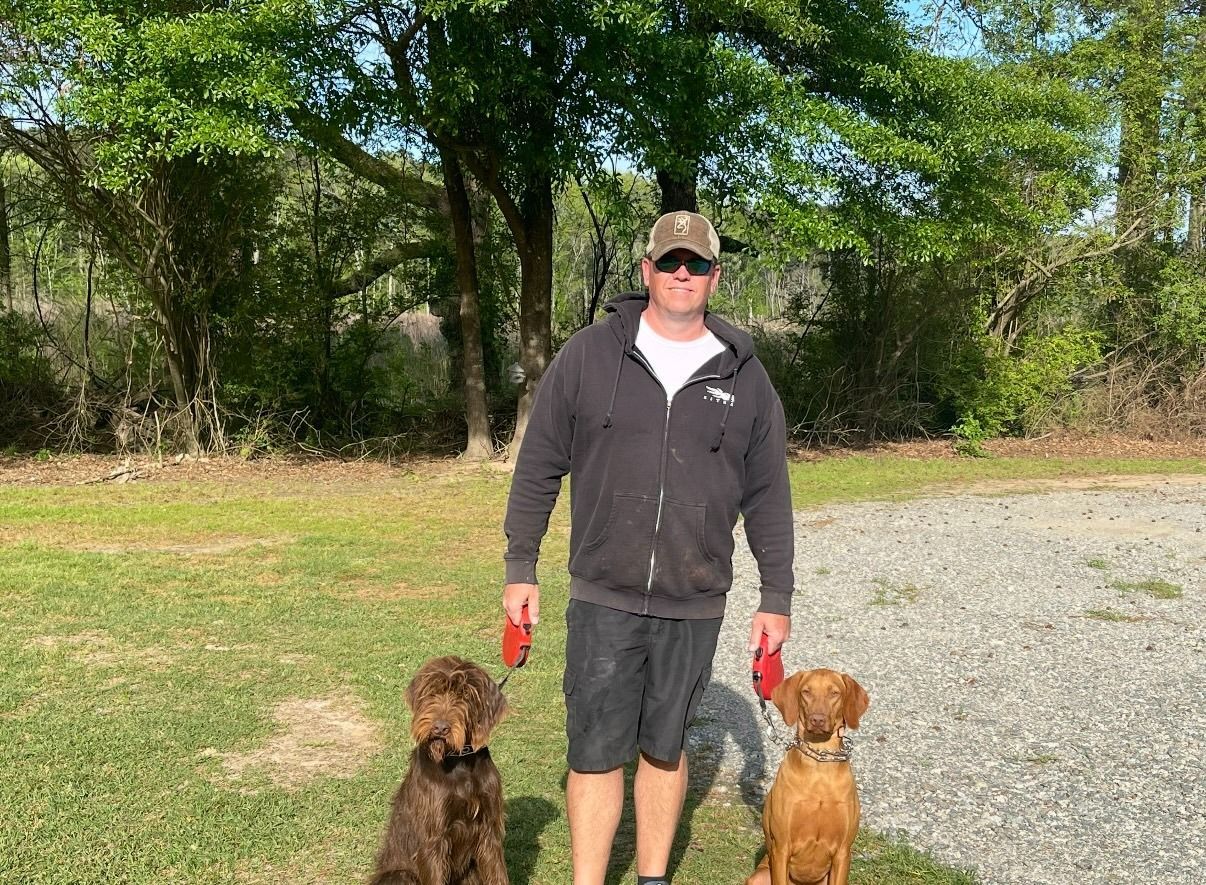 Man with two dogs on leashes, standing in a grassy area.