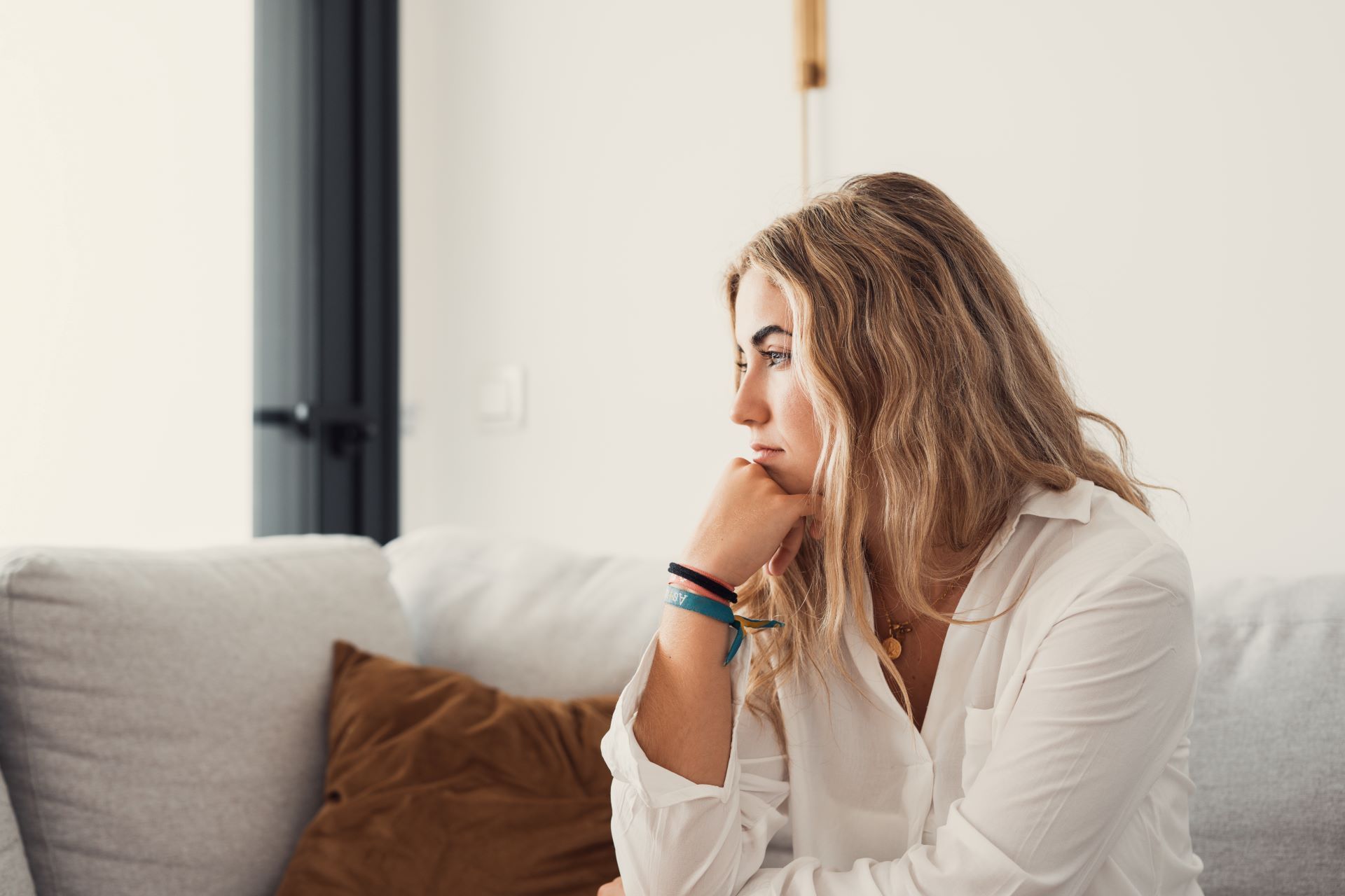A woman is sitting on a couch with her hand on her chin.
