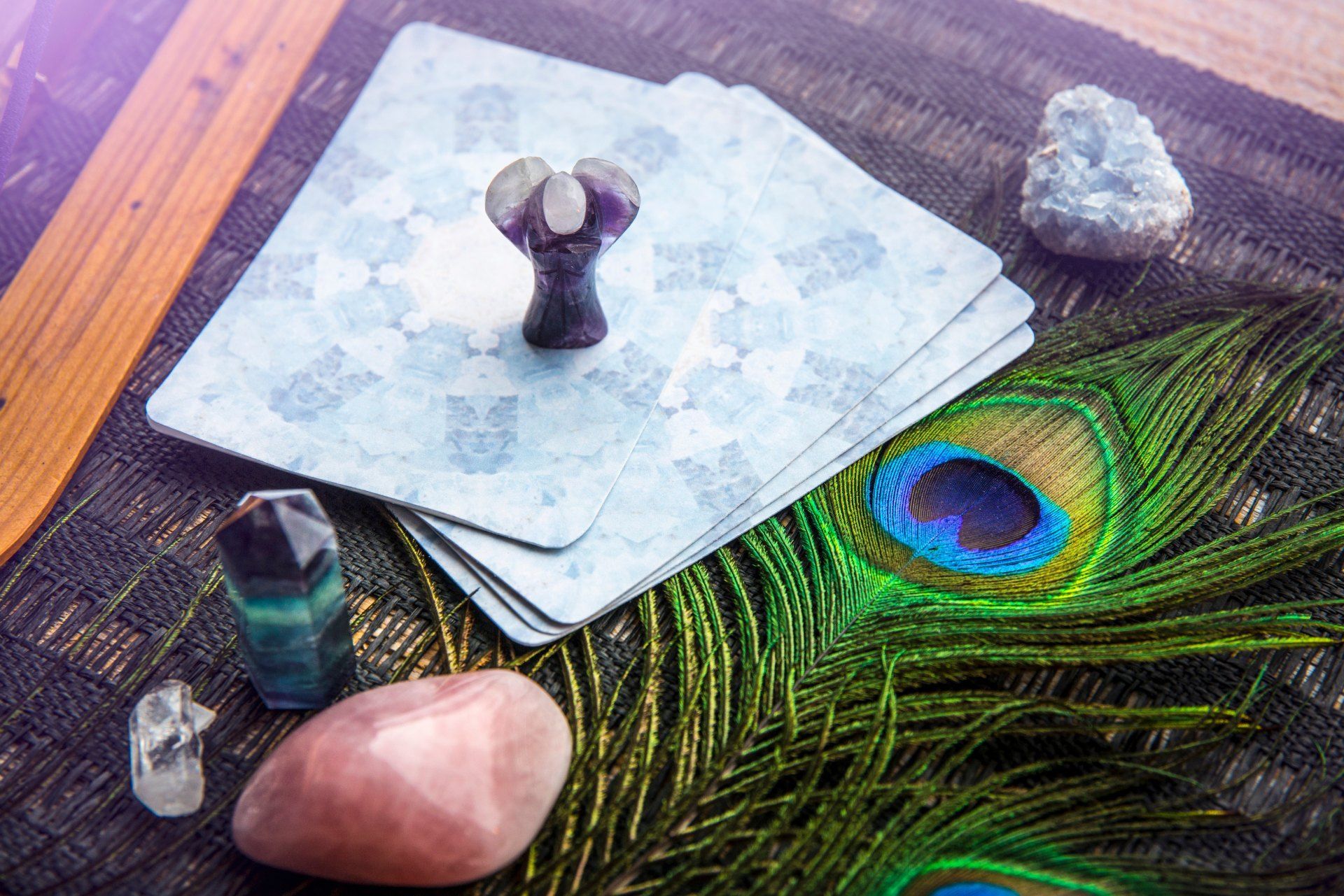A peacock feather , crystals , and tarot cards are on a table.