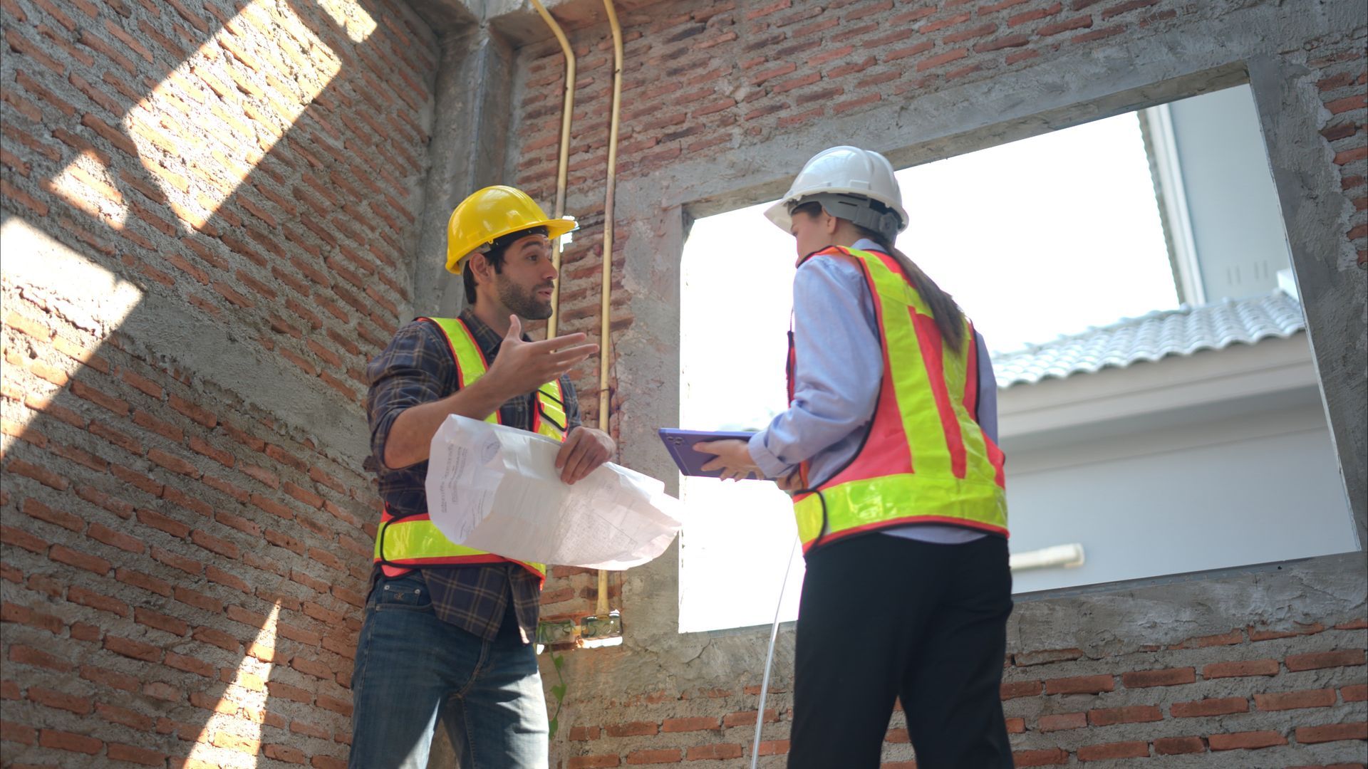 Two workers in protective gear are performing a window resizing through brick alteration.