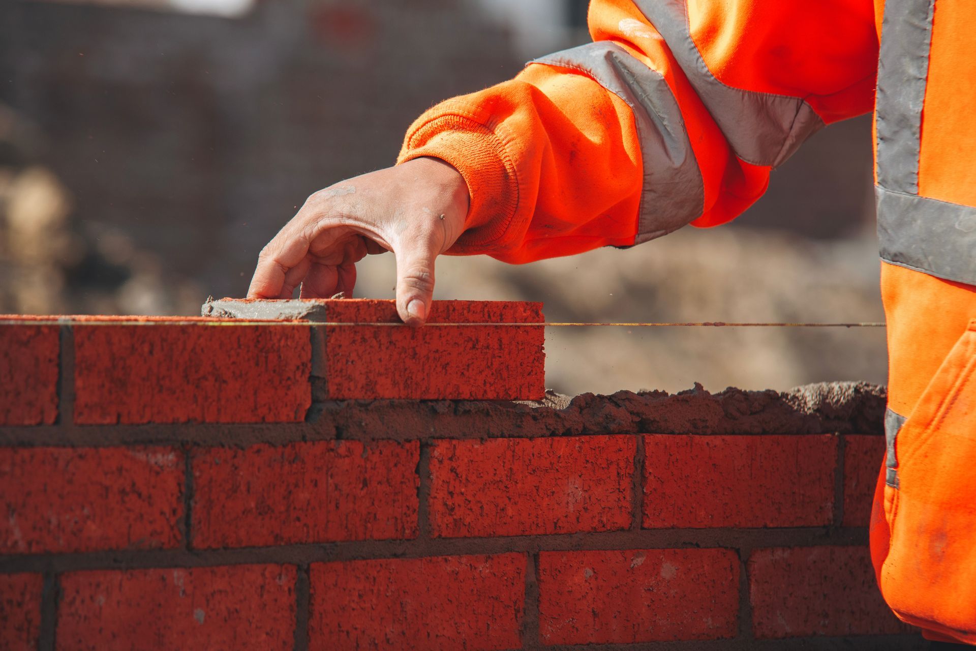 Skilled bricklayer stacking red bricks on a busy construction site.