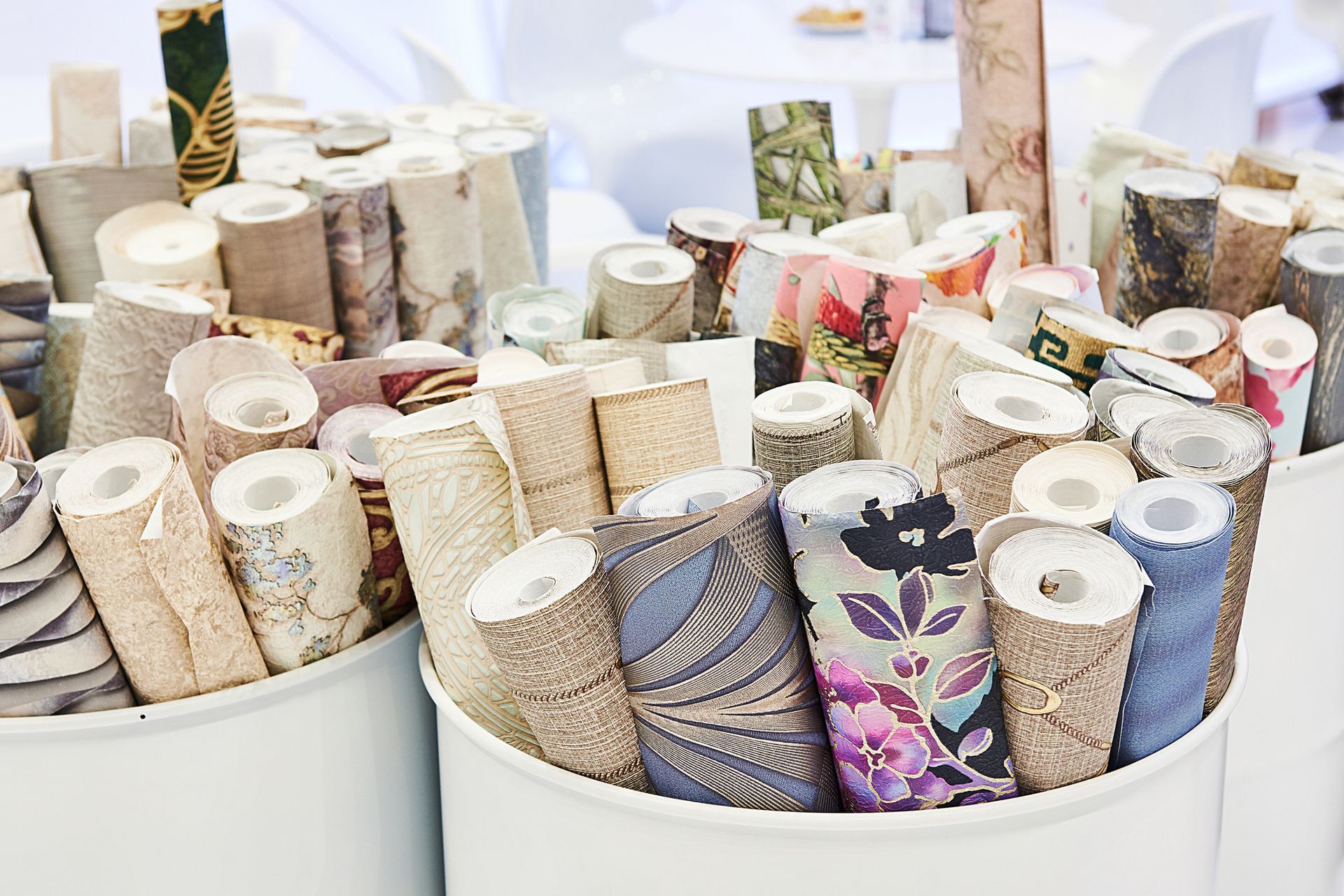 Rolls of patterned wallpaper displayed in white bins. Various colors and designs are visible.