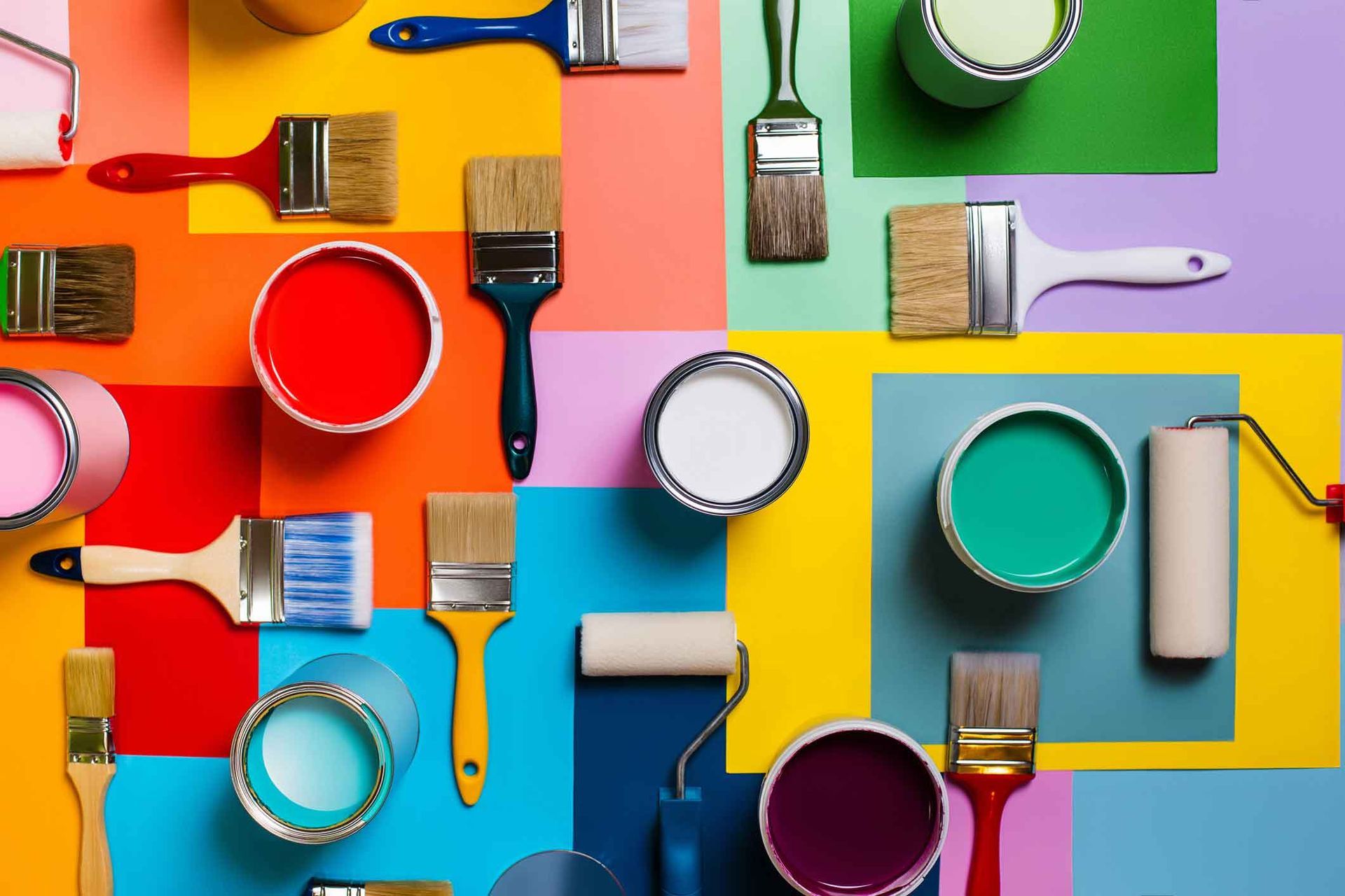 Paint cans and brushes arranged on a colorful geometric background, with hues of red, orange, yellow, green, blue, and purple.