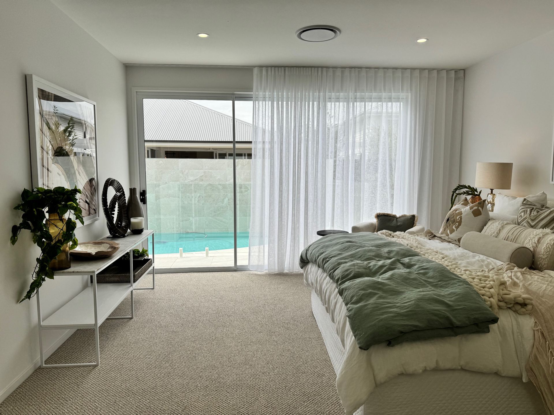 White wooden blinds partially covering a window. A vase with white flowers sits on a wooden surface in front of the blinds.