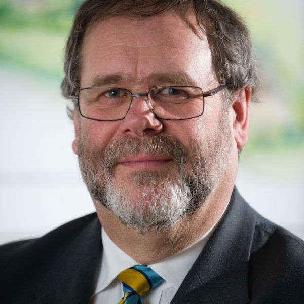A man with glasses and a beard is wearing a suit and tie