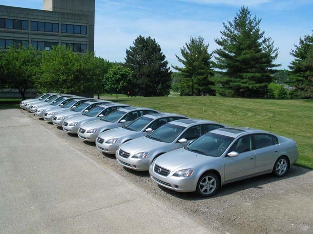 A row of silver cars are parked in a parking lot