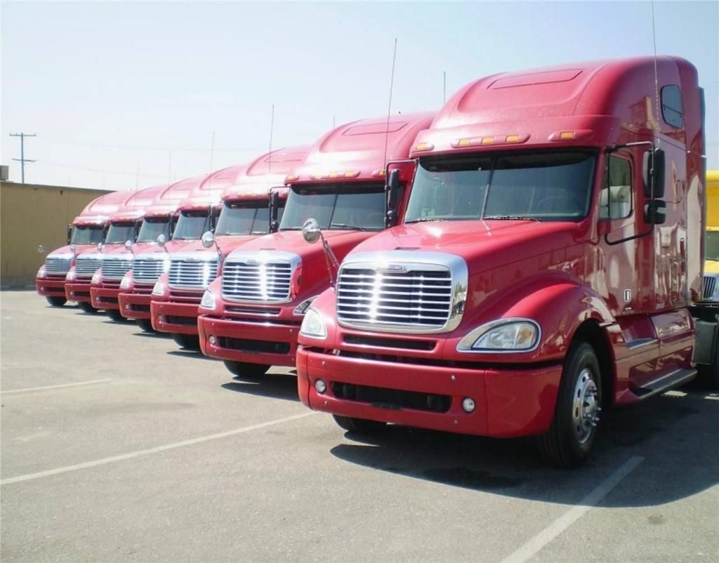 A row of red semi trucks are parked in a parking lot