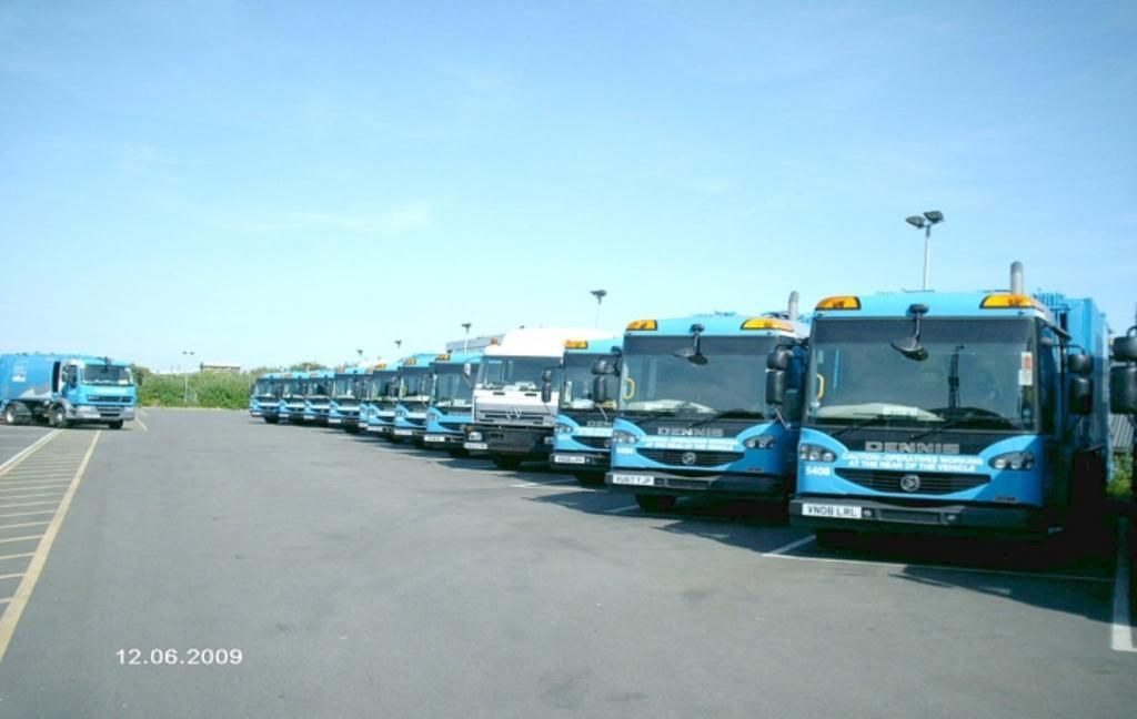 A row of blue buses are parked in a parking lot