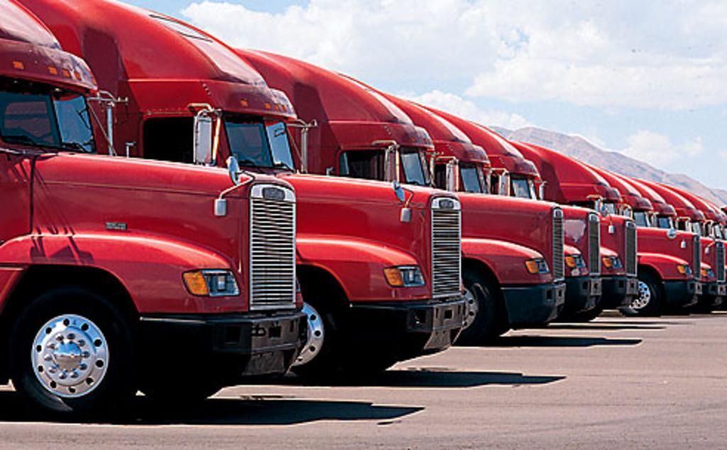 A row of red semi trucks are parked in a parking lot.