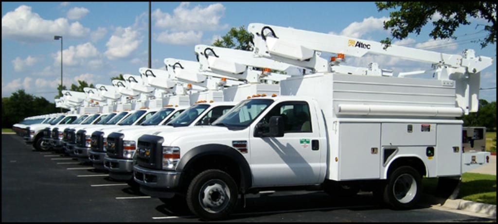 A row of white utility trucks are parked in a parking lot