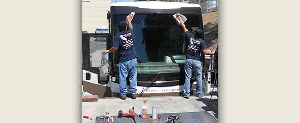 Two men are installing a windshield on a bus
