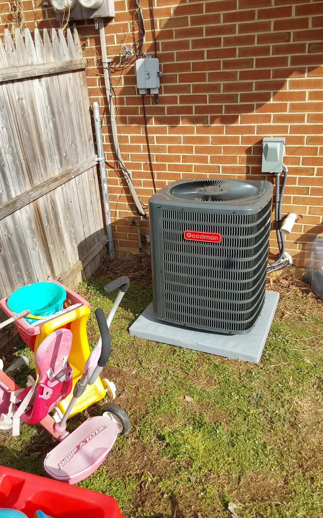 An air conditioner is sitting in the backyard next to a brick wall.