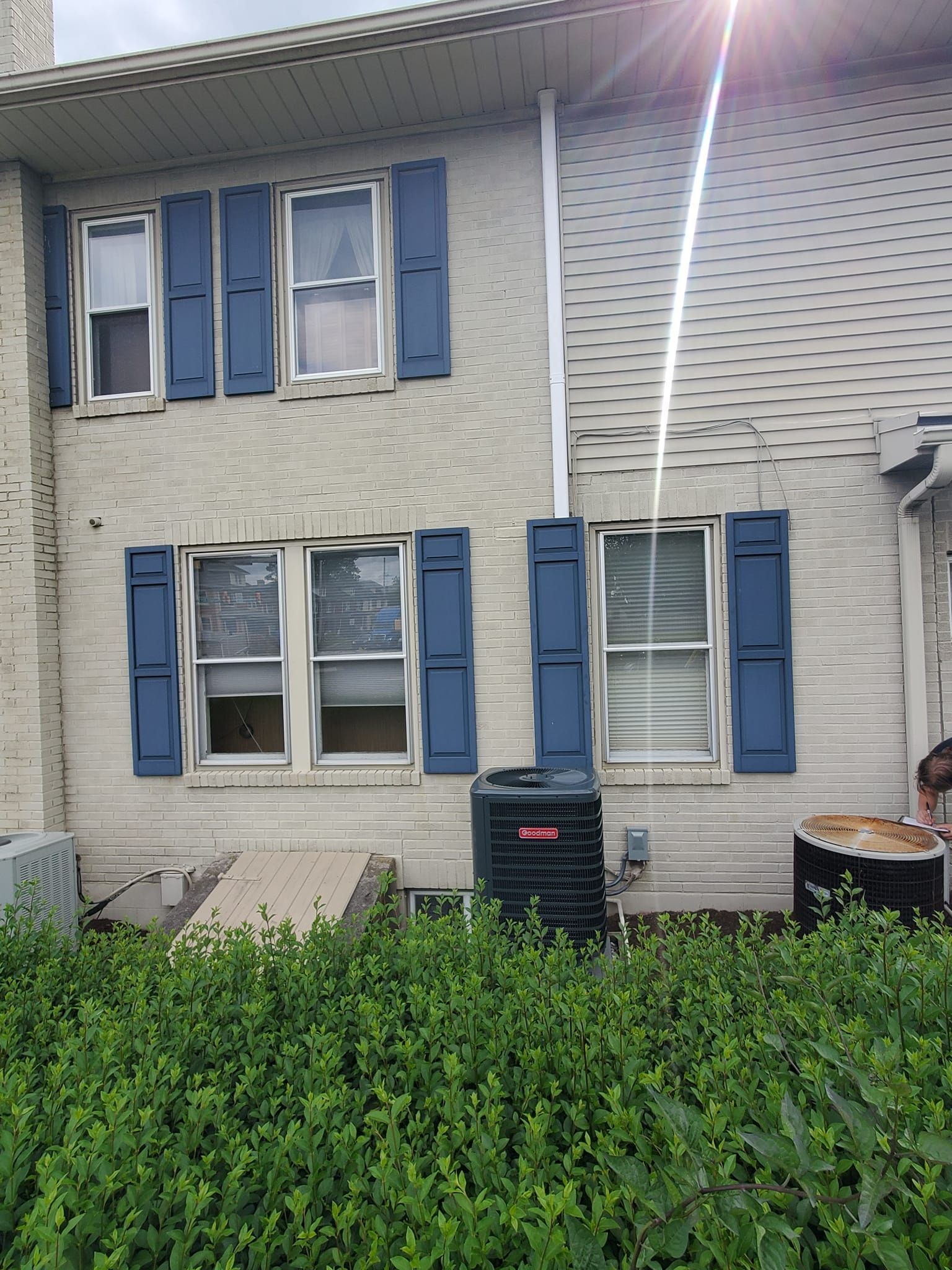 The back of a white brick house with blue shutters on the windows.