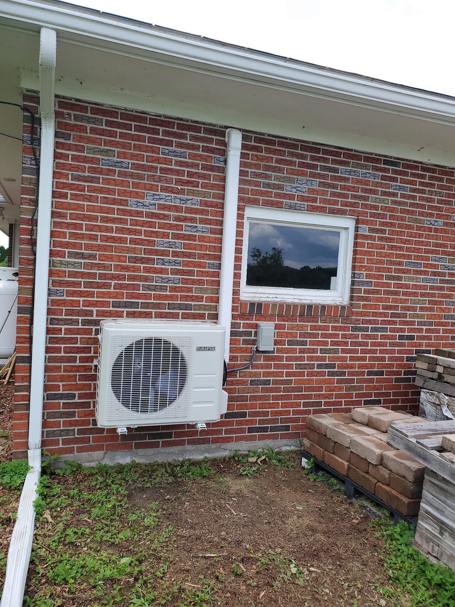 A white air conditioner is mounted on the side of a brick house.