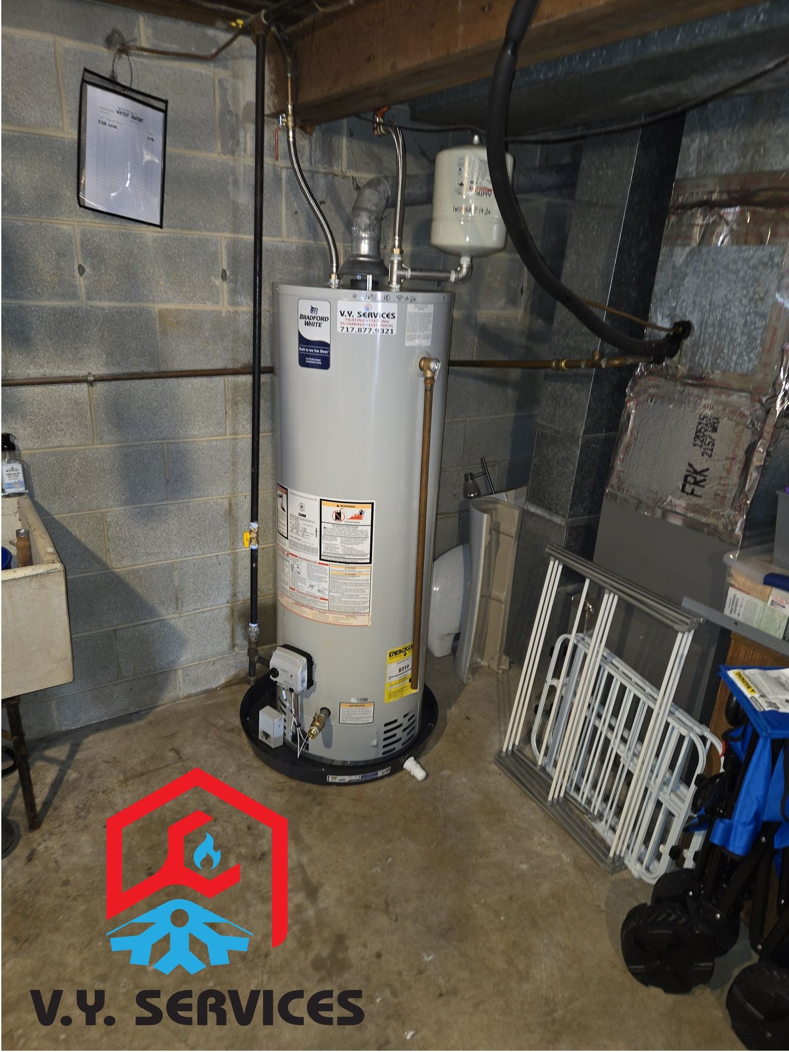 A water heater is sitting in a basement next to a sink.