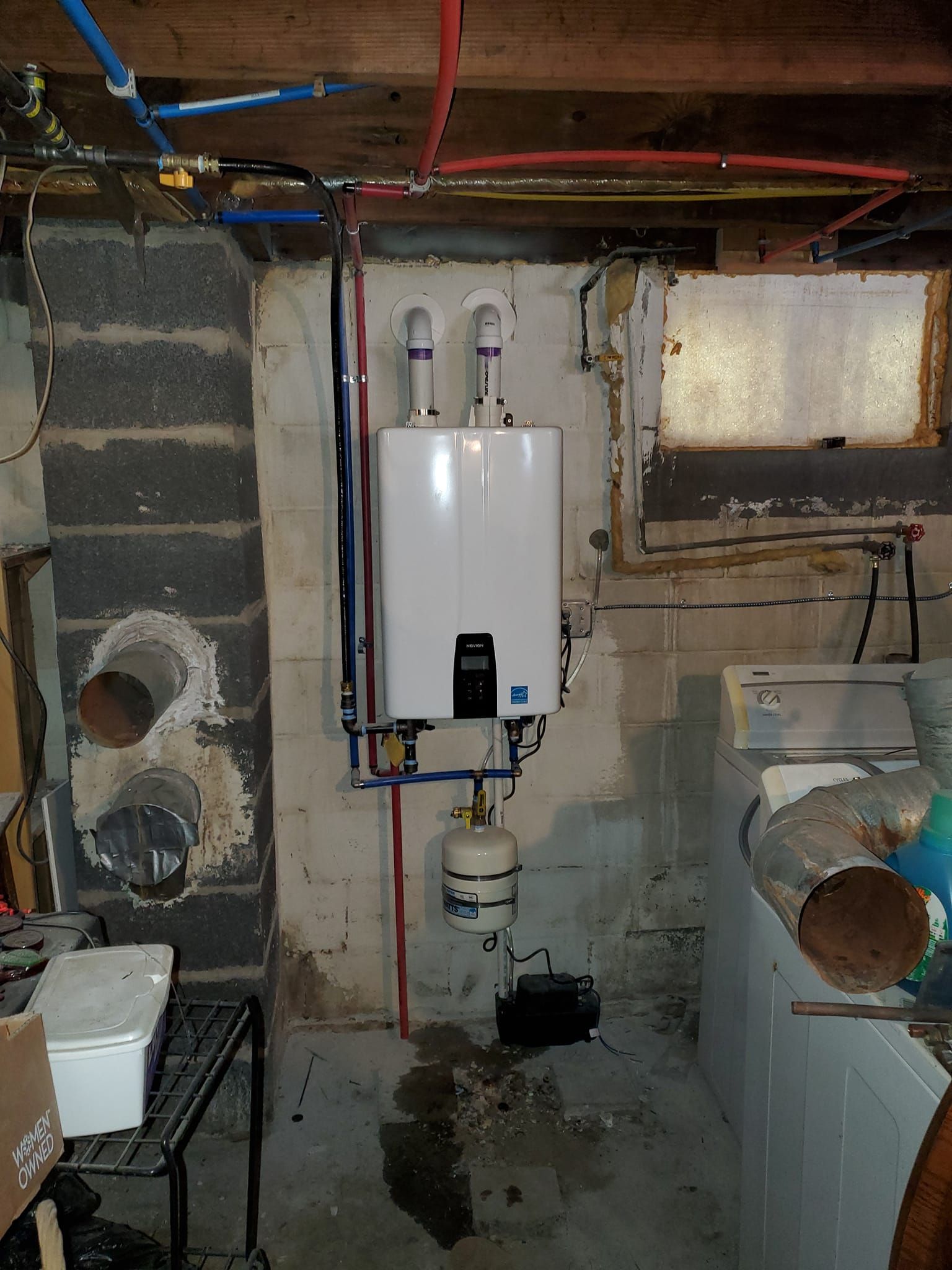 A white water heater is mounted on a wall in a basement.