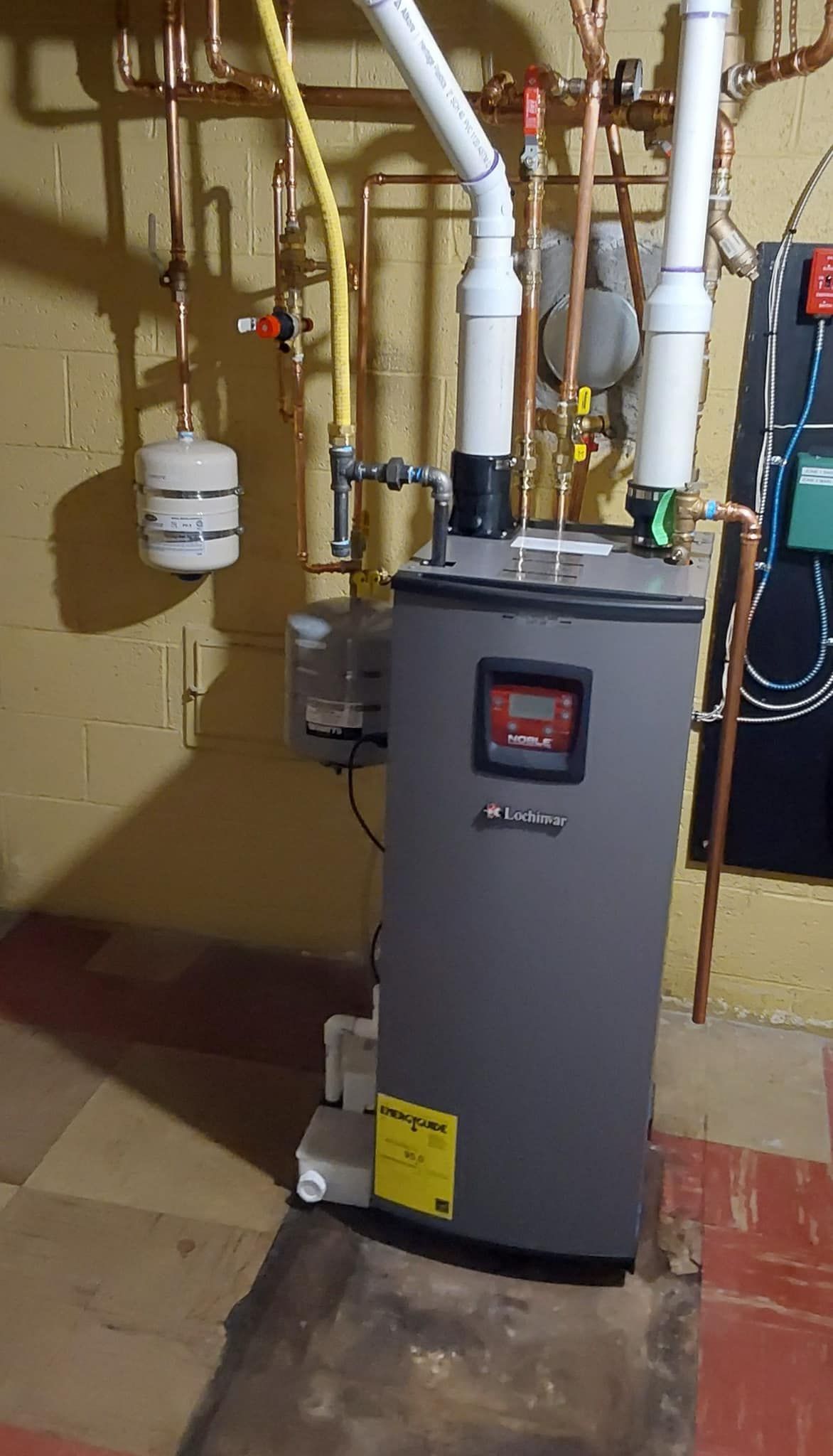 A water heater is sitting in a basement next to pipes.