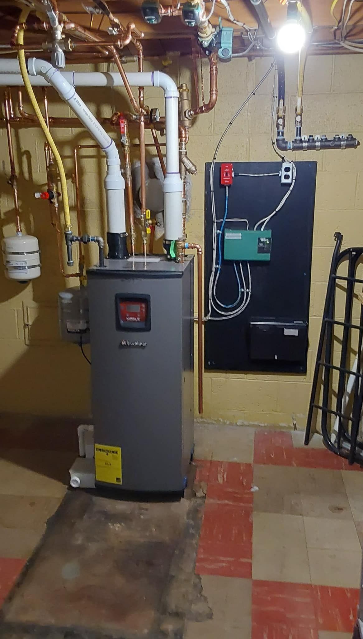 A boiler is sitting in a basement next to a wall.